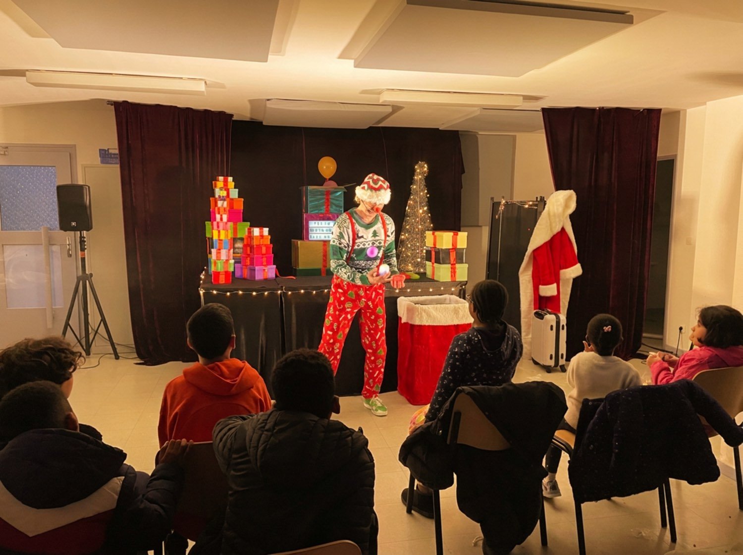 Public installé devant la tour de cadeaux, rideau noir en fond de scène.
